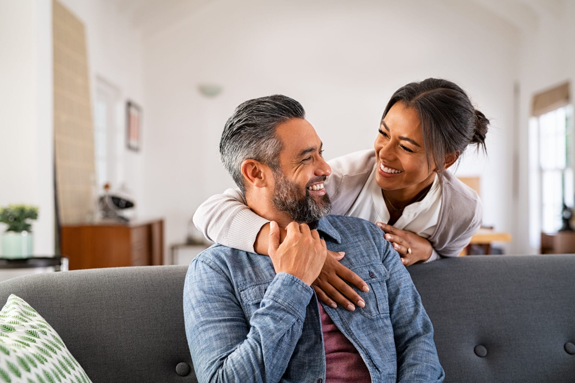 Smiling,Ethnic,Woman,Hugging,Her,Husband,On,The,Couch,From